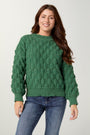 Woman wearing a green sweater and blue jeans on a plain background