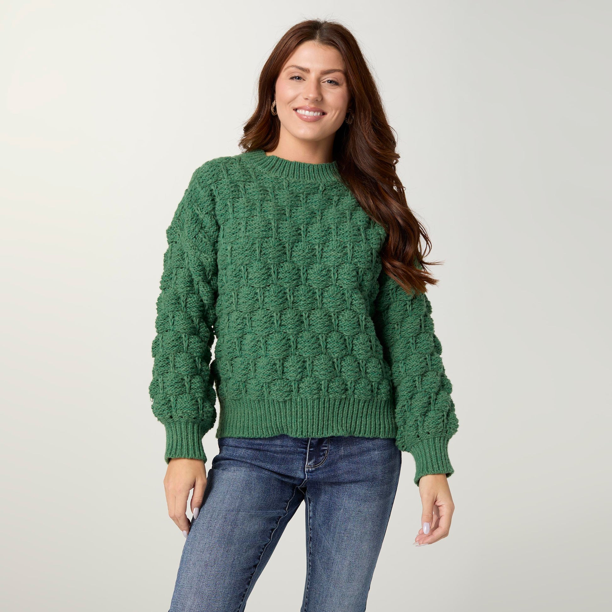 Woman wearing a green sweater and blue jeans on a plain background