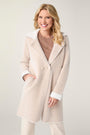 Woman wearing a beige coat with white trim on a plain background