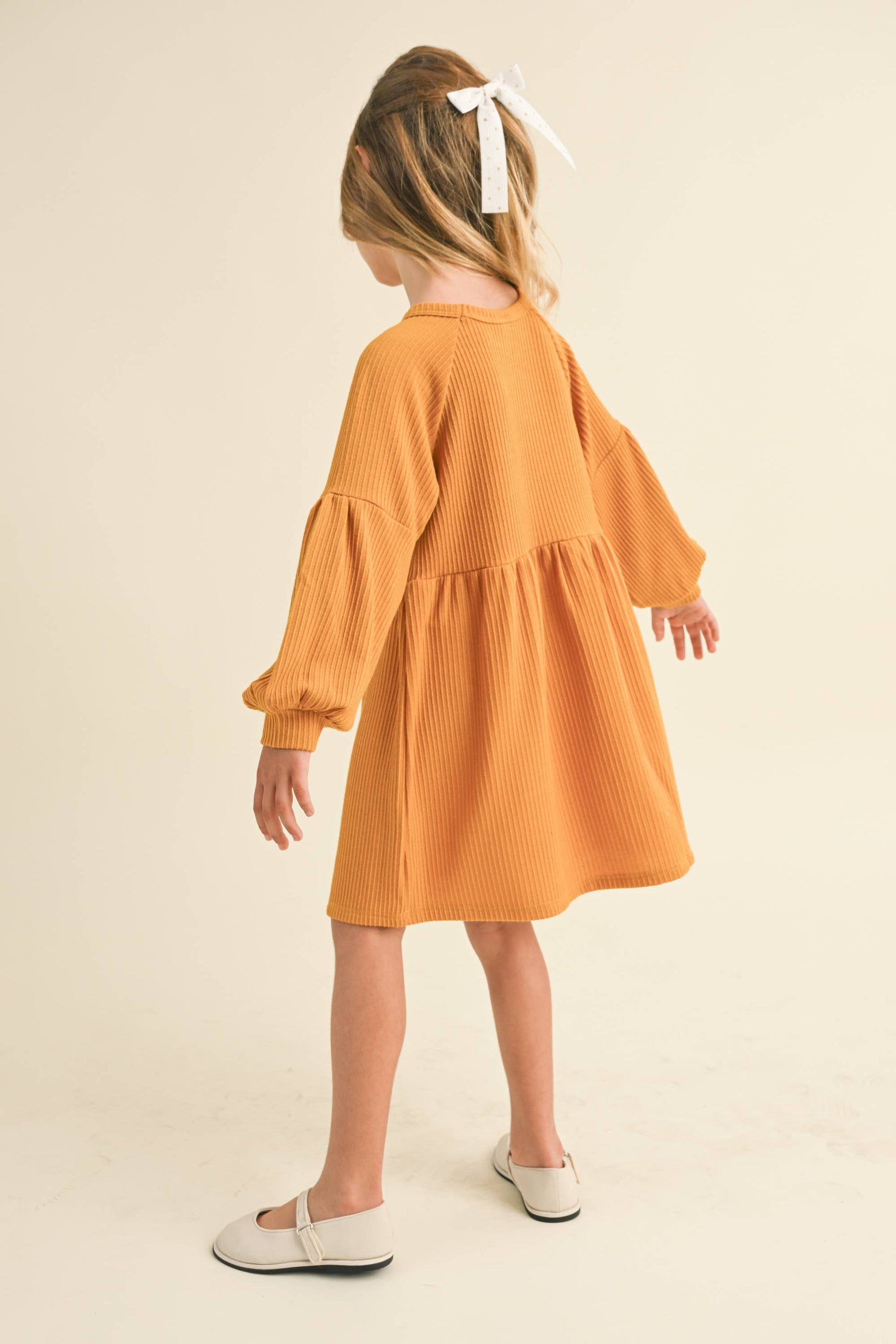 Child wearing a mustard yellow dress with ruffled sleeves on a beige background