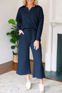 Woman wearing a navy blue outfit standing in a room with a plant and fireplace.