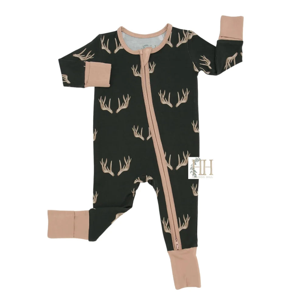 A baby long-sleeve footed sleeper in black with a tan deer antler pattern, featuring tan cuffs and a tan front zipper, shown on a white background.