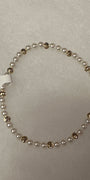 A beaded stretch bracelet featuring small white pearls separated by polished gold-toned round beads, shown on a light gray textured background with a white product tag attached.