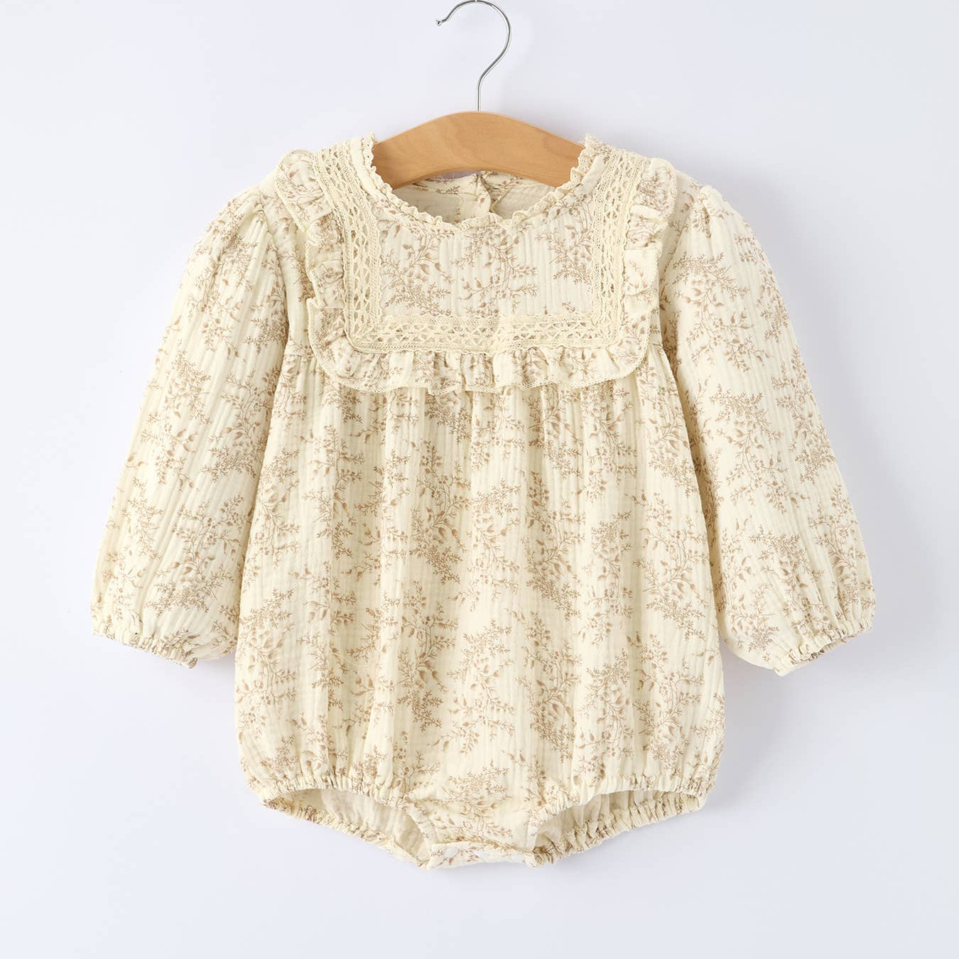 Baby romper with lace details on a hanger against a white background