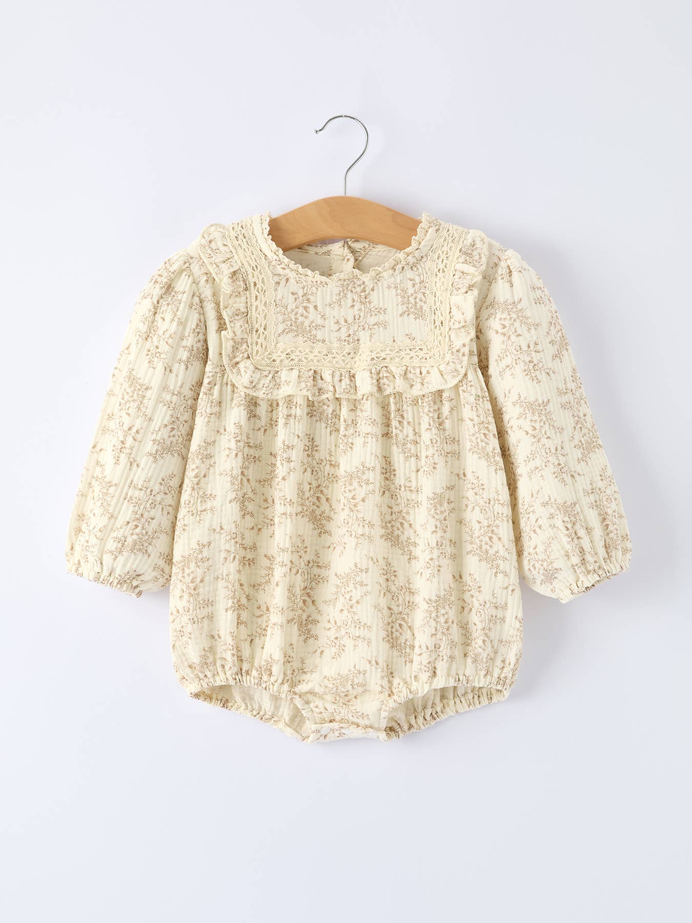 Baby romper with lace details on a hanger against a white background