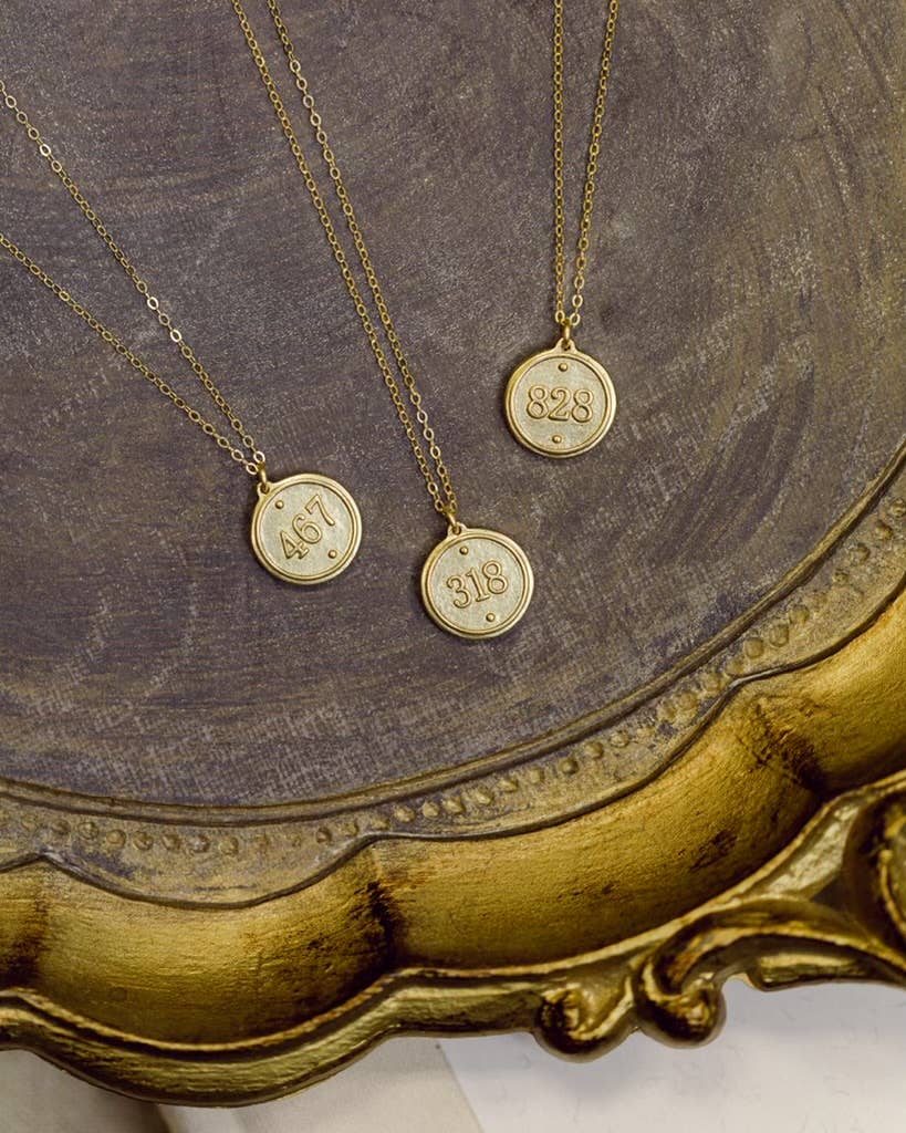 Three gold necklaces with round pendants on a decorative gold frame.