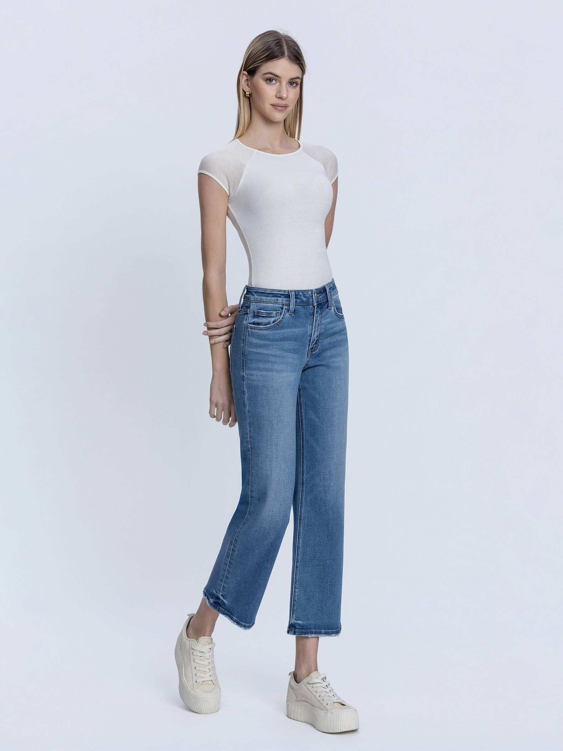 Woman wearing a white top and blue jeans on a light gray background