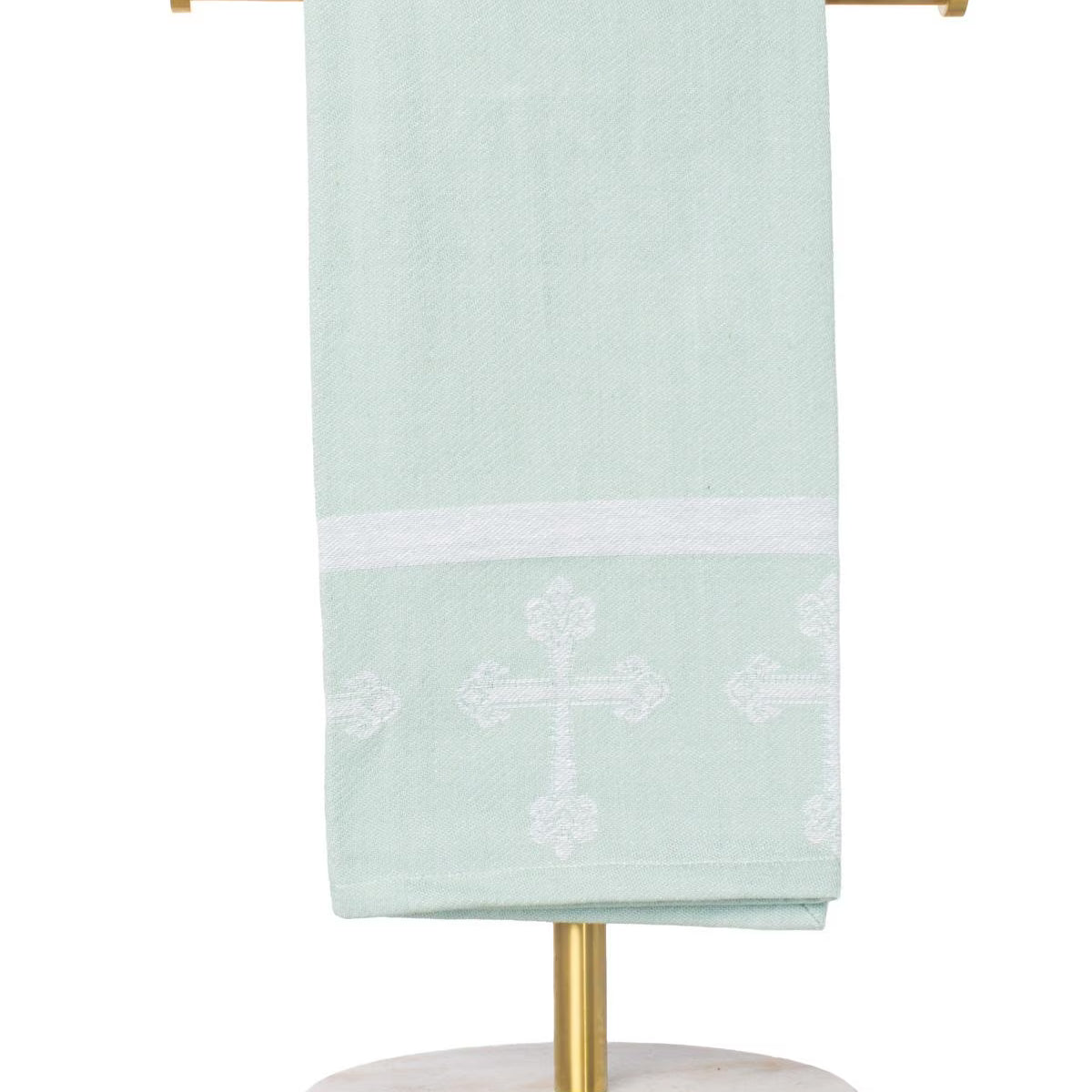 Light green towel with white cross design on a gold towel rack against a white background
