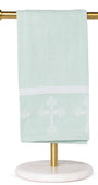 Light green towel with white cross design on a gold towel rack against a white background
