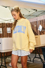 Woman wearing a yellow sweatshirt with 'Dally Dally' text in a casual setting.