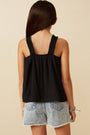 Woman wearing a black sleeveless top and denim shorts on a beige background