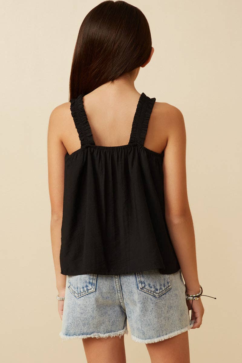 Woman wearing a black sleeveless top and denim shorts on a beige background