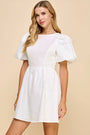 Woman wearing a white dress with ruffled sleeves against a beige background