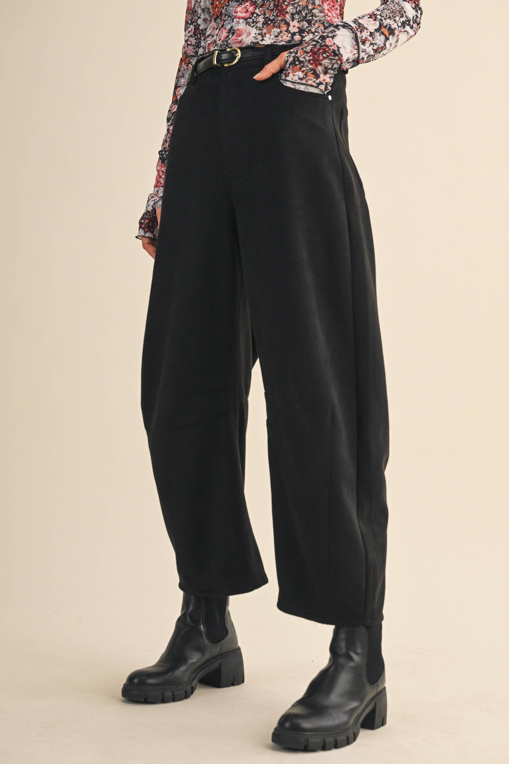 Person wearing black high-waisted pants with a floral blouse on a beige background