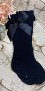 Black sock with a bow on a textured surface with flowers in the background