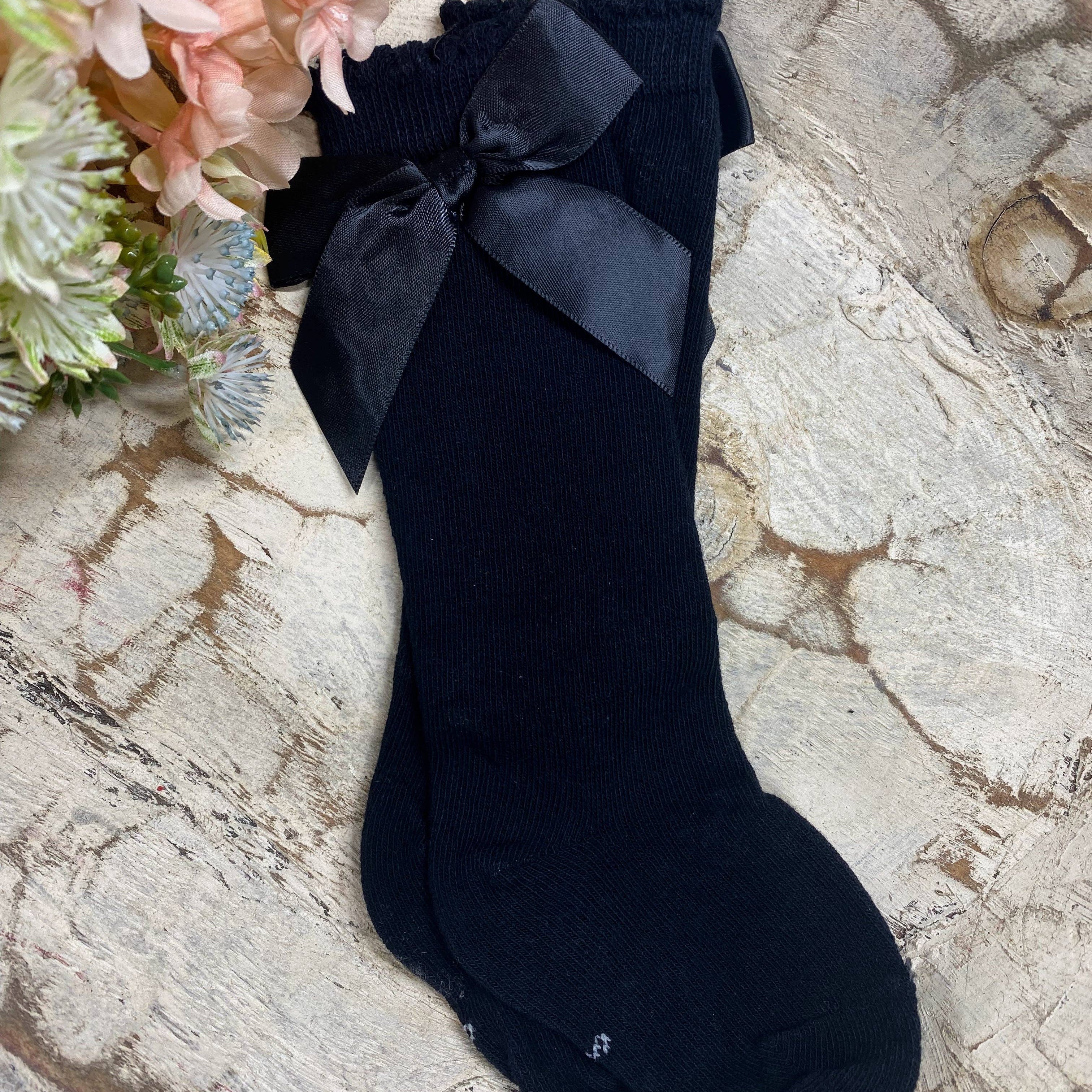 Black sock with a bow on a textured surface with flowers in the background