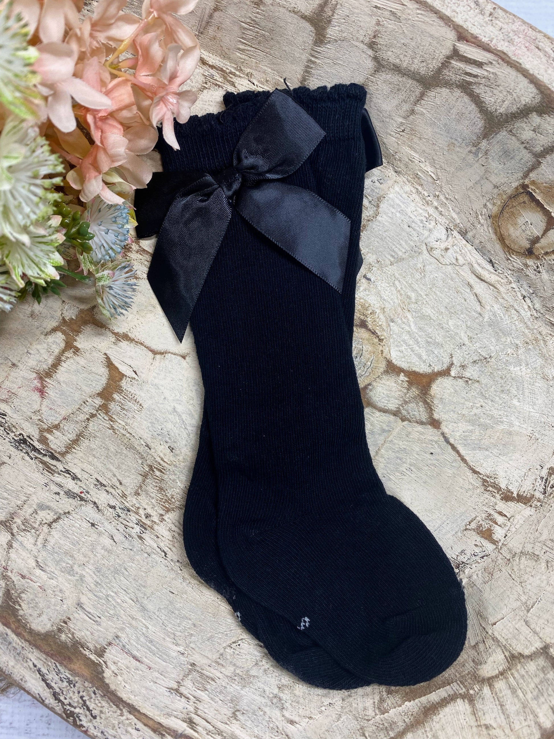 Black sock with a bow on a textured surface with flowers in the background