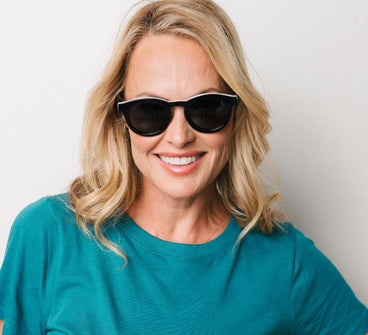 Woman wearing sunglasses and a teal shirt against a plain background