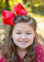 Young girl with a large red bow in her hair, smiling outdoors.