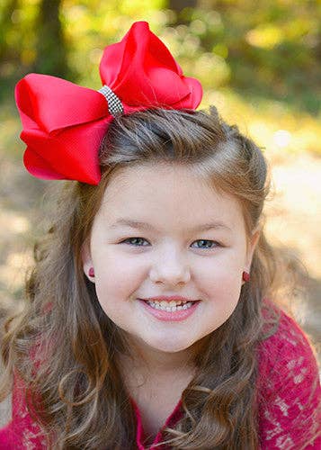 Young girl with a large red bow in her hair, smiling outdoors.