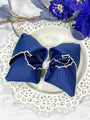 Blue hair bow with white trim on a decorative plate with flowers in the background