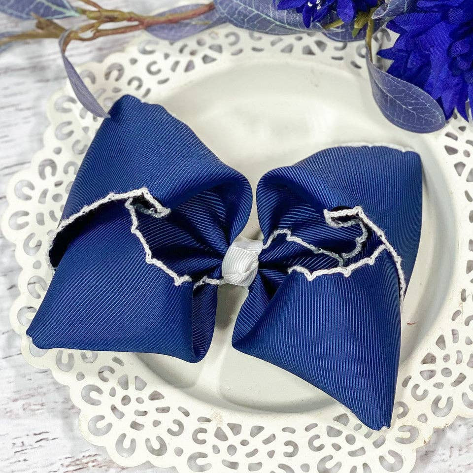 Blue hair bow with white trim on a decorative plate with flowers in the background