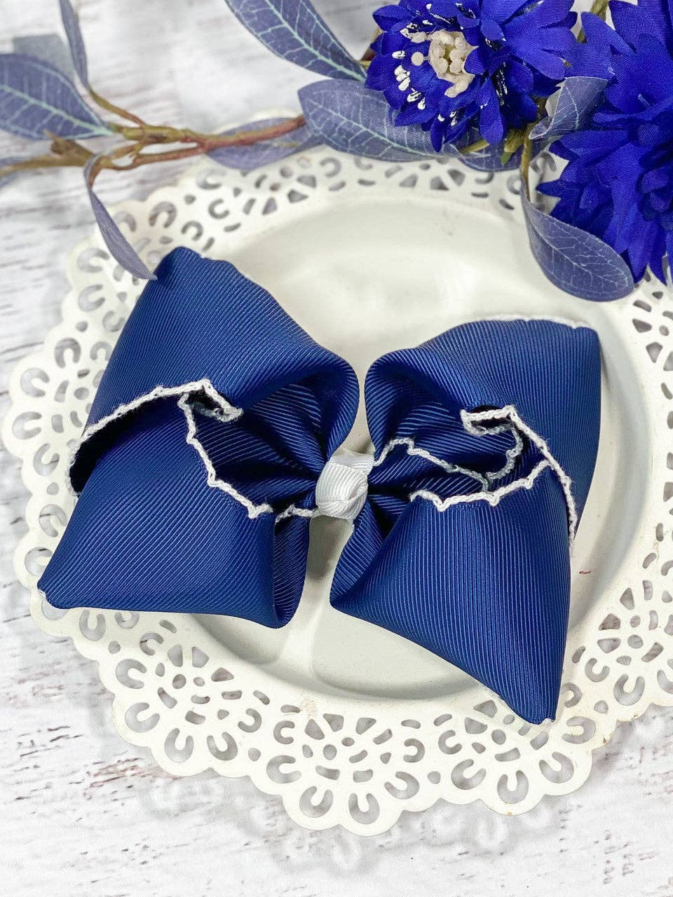Blue hair bow with white trim on a decorative plate with flowers in the background