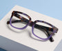 purple tortoiseshell glasses on a white surface with a light blue background