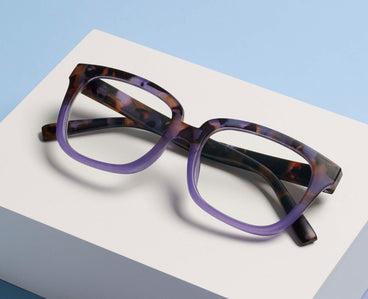 purple tortoiseshell glasses on a white surface with a light blue background