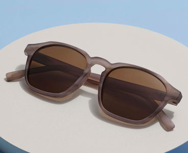 Brown sunglasses on a light beige surface with a blue background
