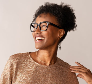 Woman wearing glasses and a sparkly top against a plain background