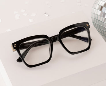 Black glasses on a white surface with a disco ball in the background