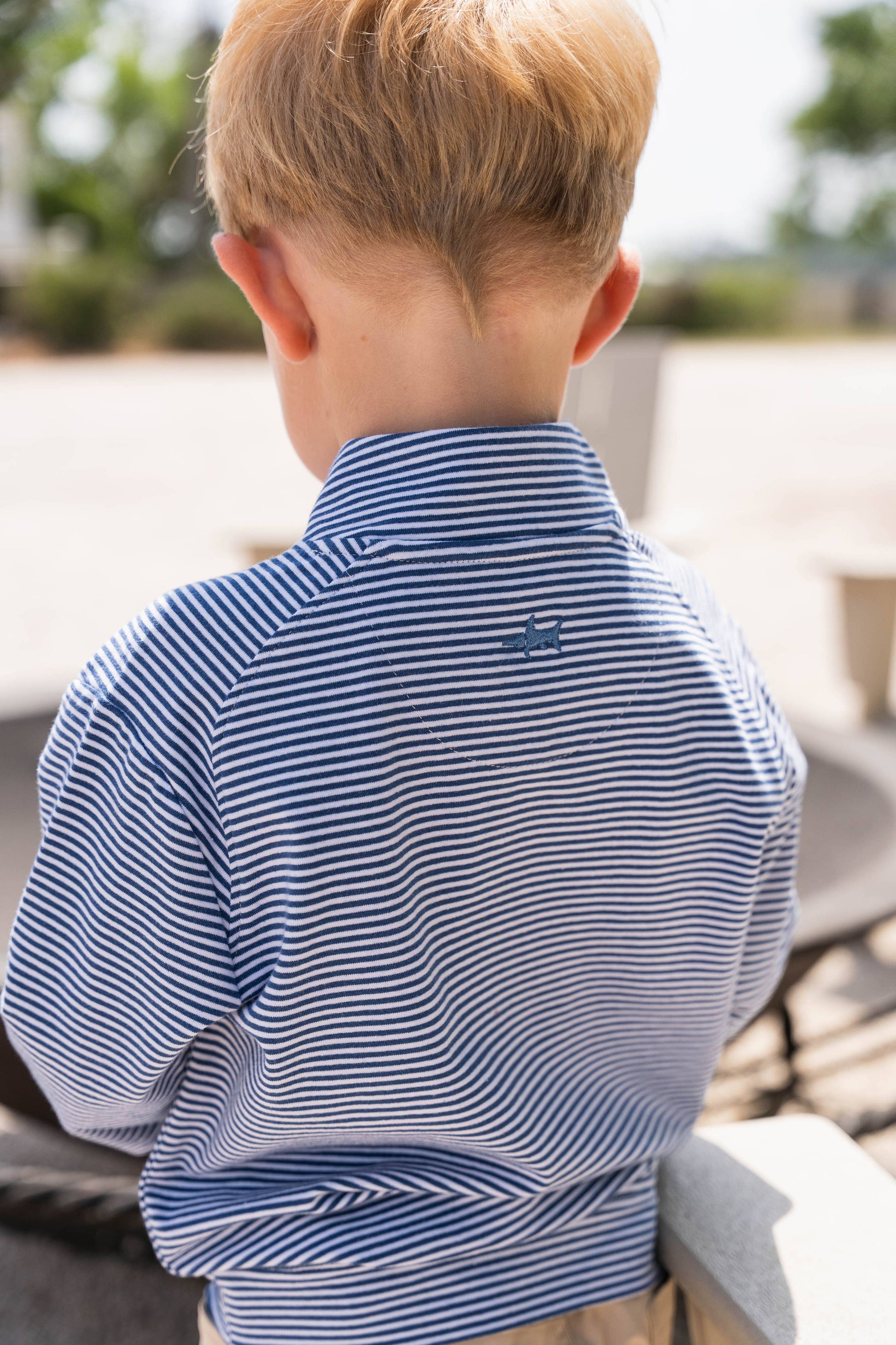 Child wearing a blue striped shirt with a logo, standing outdoors.