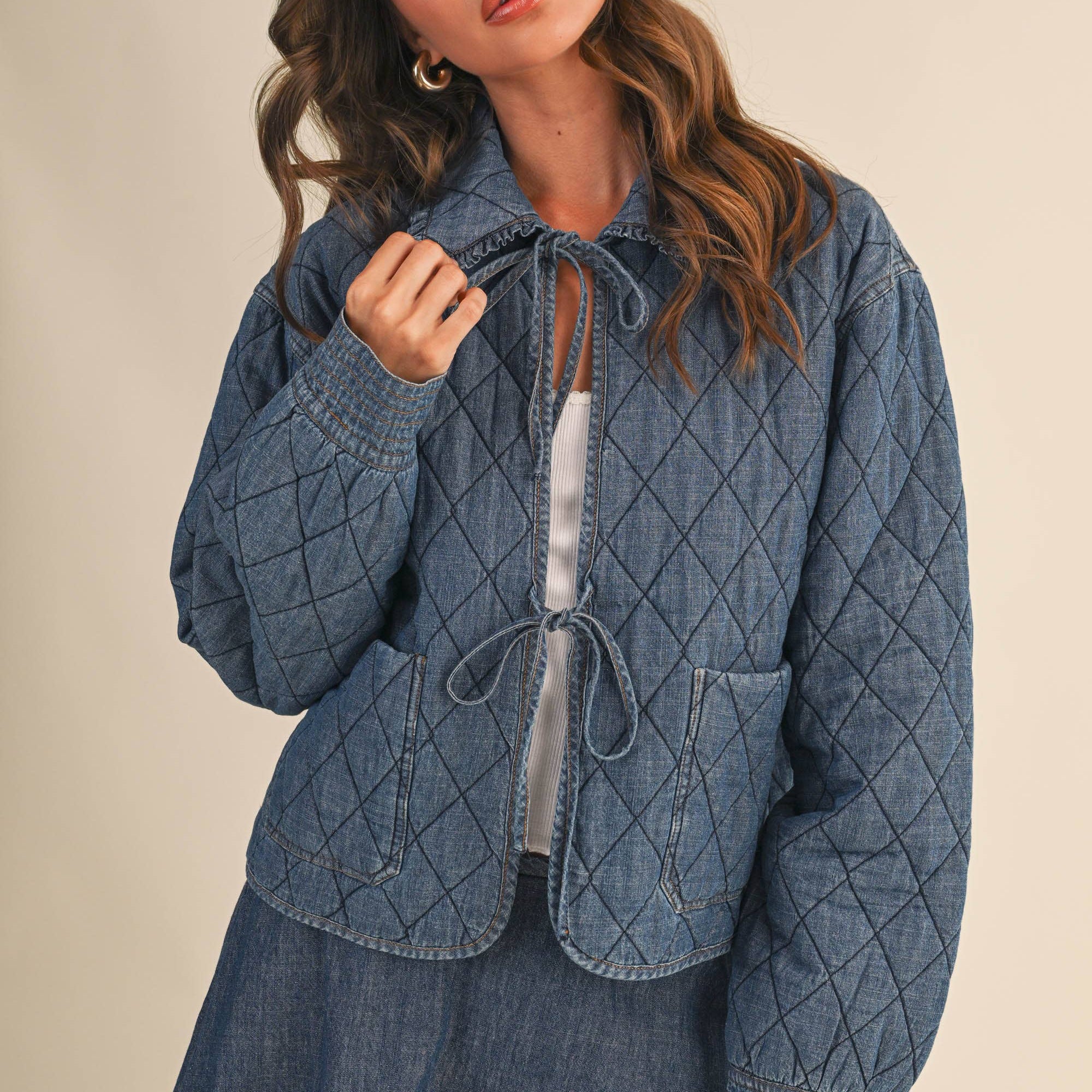 Woman wearing a blue quilted jacket with a skirt against a beige background