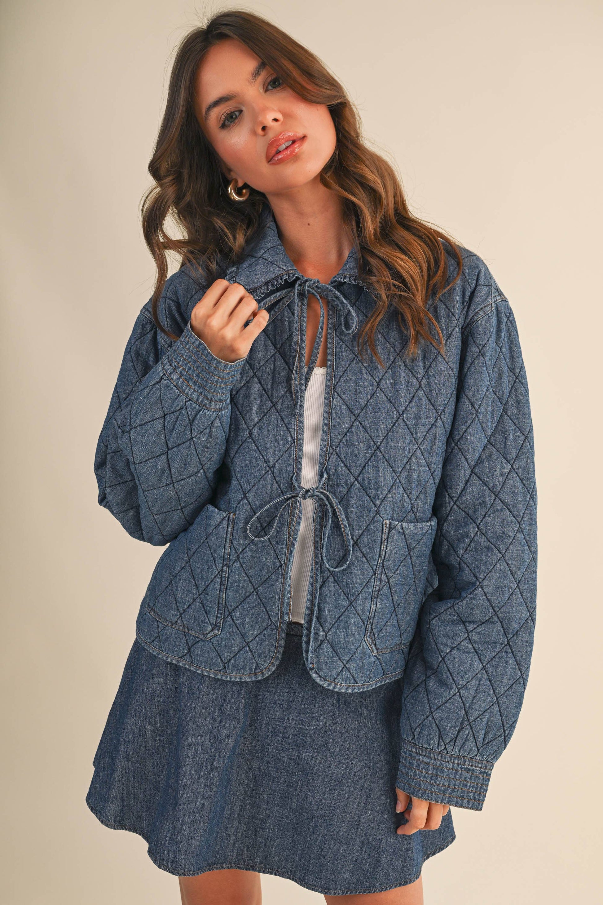 Woman wearing a blue quilted jacket with a skirt against a beige background