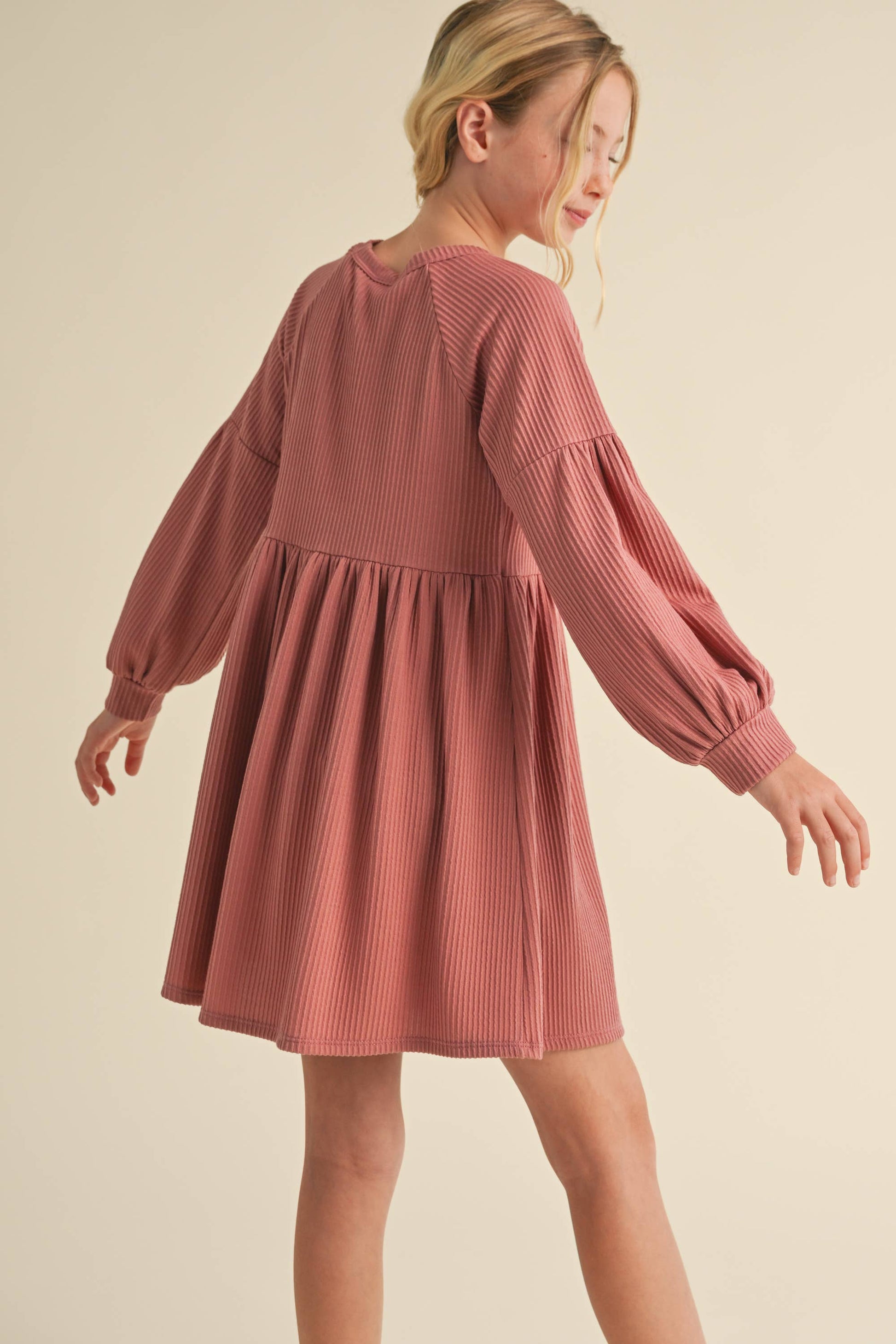 Woman wearing a pink dress with long sleeves on a beige background