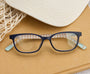 Blue eyeglasses on a textured surface with a hat in the background