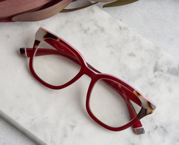 Red eyeglasses with tortoiseshell accents on a marble surface