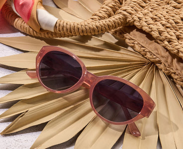 Sunglasses with pink frame and dark lenses on a white background on a tan beach themed background