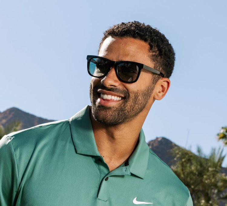 Man wearing sunglasses and a green shirt with a mountainous background