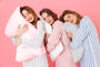 Three women lying on different types of pillows against a pink background