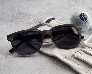 Black sunglasses on a white golf glove with a golf ball in the background