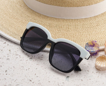 Black sunglasses with white frame on a textured surface with a straw hat and seashells.