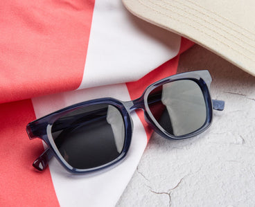 Sunglasses on a red and white striped fabric with a beige hat in the background