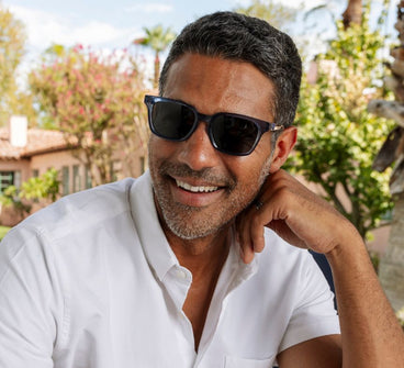 Man wearing sunglasses and a white shirt outdoors with trees in the background