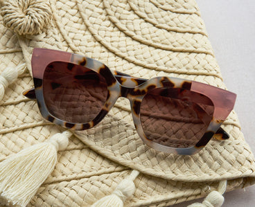 Tortoiseshell sunglasses with pink detail on a textured beige surface