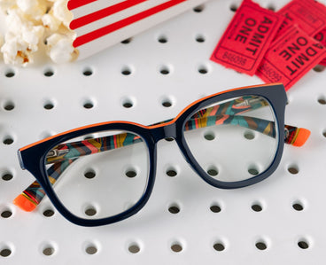 Colorful eyeglasses on a perforated surface with popcorn and movie tickets in the background