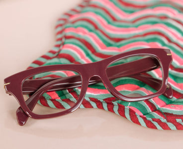 cherry red eyeglasses on a red and green striped fabric background