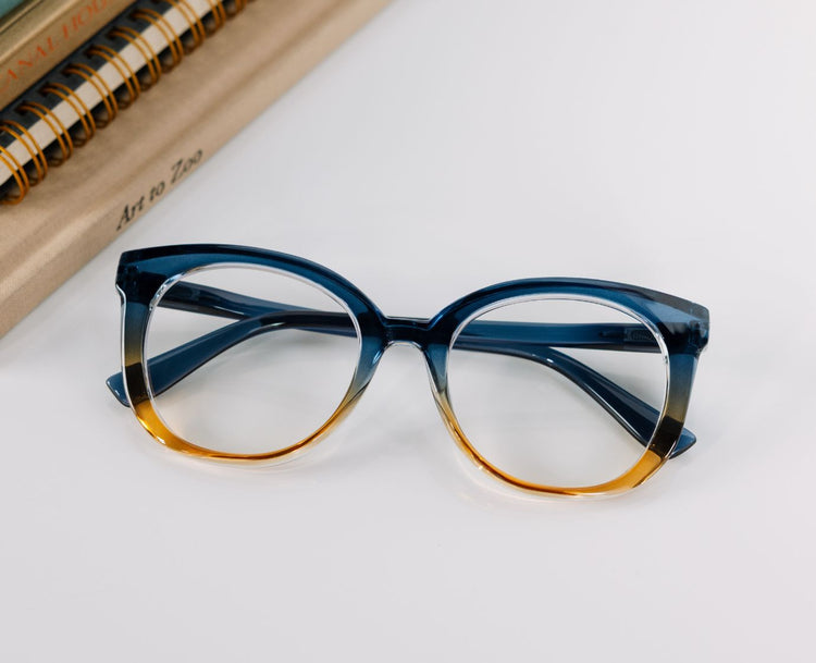 Blue and gold eyeglasses on a white surface with a notebook in the background