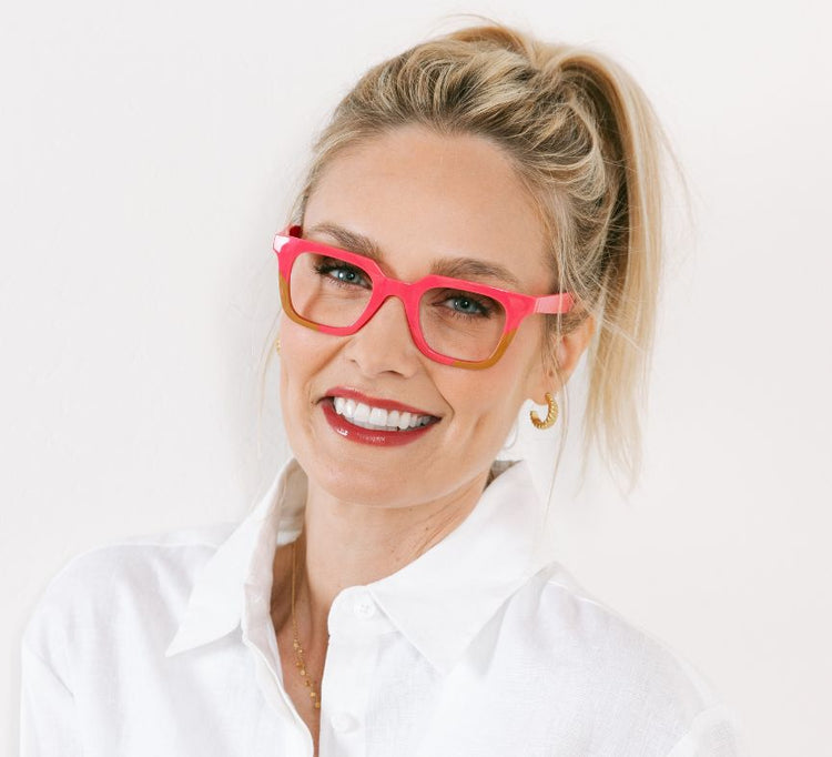 Woman wearing bright pink glasses and a white shirt against a light background